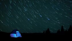 The glow from a tent matches the blue streaks of stars moving across the night sky of Big Sur. Stock Footage