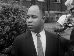 B/W 1950s Black male official talking to camera in front of school / pro-segregation protests Stock Footage