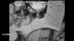 1937: BERLIN, NAZI GERMANY: CU Cake onto plate on table w/ sugar, cream. CU Reduction in pan being poured over plated foul. Men drinking beers at outdoor tables, tram passing BG. Cafe menu in window. Instructional Video
