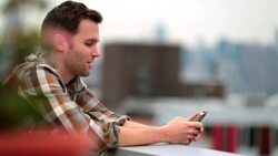 Hip young man on Brooklyn rooftop texts on smartphone and smiles (dolly-shot) Stock Footage