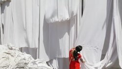 A woman in a red sari stretches freshly dyed fabrics hanging out to dry. Stock Footage