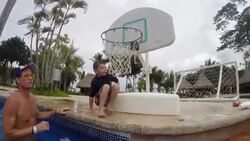 Father and two children play pool basketball at resort pool and then father splashes camera Stock Footage