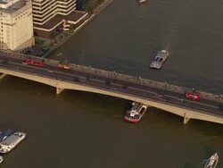 Aerial zoom in to traffic and pedestrians crossing London Bridge on Thames with tour boats passing underneath / London Stock Footage