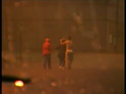 MS view from inside car of 3 people crossing road during torrential downpour, man takes off top and uses it to shield woman, at night, USA Stock Footage