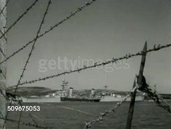 1942: FRANCE BIZERTE NAVY BASE: LS Rows of French Naval officers standing on submarines docked in harbor. WS Destroyer ship in harbor, barbed wire FG. MS Sailors saluting Admiral coming on board. INT MS Admiral & officer looking at map. Instructional Video
