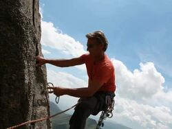 Boom across to man leading rock climb, placing protection Stock Footage
