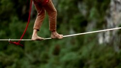 Man traverses highline stretched above waterfall, valley Stock Footage