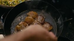 In restaurant kitchen, chef splashes grease over sizzling scallops in iron skillet in slow motion Stock Footage