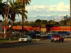 WS, New BNSF train engines and one old Santa Fe train engine together pulling through Needles train station, traffic on street in foreground, California, USA Stock Footage