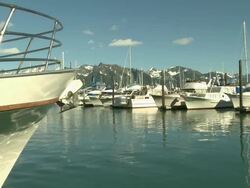 "View of boats in Seward Small Boat Harbor, CU of boat's bow in foreground, with rocky mountain top in Chugach National Forest, with partial snow, Seward, Kenai Peninsula, Alaska, blue skies." Stock Footage