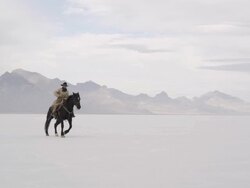 Cowboy sitting on horse starting to run on salt flats. Stock Footage