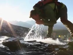 Hiker crosees creek, has drink, then continues up ridge Stock Footage