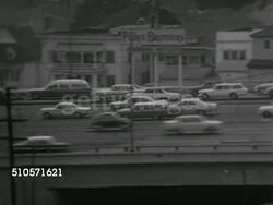 1965: FREEWAY TRAFFIC: HA WS REVERSE PAN Elevated city highway w/ cars moving both directions, WS (POV Front of moving vehicle) IN bumper-to-bumper traffic on access road leading to expressway. AERIAL Traffic. HA Angled WS Four lane traffic. Instructional Video