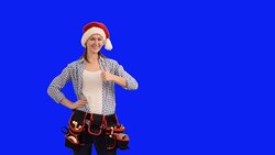 slender young woman construction worker in a cap of Santa Claus shows a copy space  on a blue background Stock Footage
