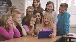 Elementary school aged children working on digital media tablets with teacher in classroom Stock Footage