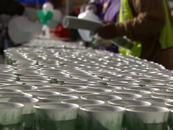 Cups of water line a table near volunteers with plastic jugs. Stock Footage