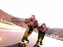 OVEREXPOSED CANTED tracking shot two skateboarders with helmets speeding on mountain road Stock Footage