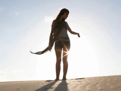 Teenage girl dances in sand dunes,sun behind Stock Footage