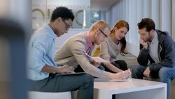Creative young business people write and discuss ideas around white-board table in large corporate office common area (dolly shot) Stock Footage