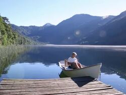 Man relaxes in rowboat on mtn lake, uses digital tablet Stock Footage