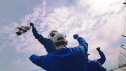 Woman in racing helmet waves checkered flag; blue racing team lifts woman up, celebrates stock car victory Stock Footage
