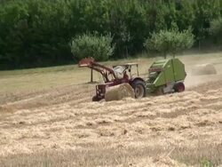 MS Tractor passing through grass field with bale of straw in field / Serrig, Rhineland-Palatinate, Germany Stock Footage