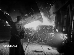 1940s: STEEL MILL:  LA MS Smoke stacks. INT WS Male operating blast furnace in steel mill, pouring liquid steel, working w/ rods. Production, war effort, WWII Instructional Video