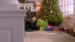 Excited young boy shakes present intently in front of Christmas tree (dolly-shot) Stock Footage