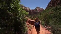 Mother and son hike past while walking on a dusty trail surrounded by rocky mountains in Zion National Park Stock Footage