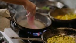 Chef places fish fillet on iron skillet over crowded stove top in restaurant kitchen Stock Footage
