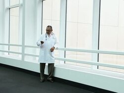 WS Physician walking into lobby stops at large bank of windows and talks on his cell phone / Seattle, Washington, USA Stock Footage