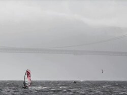 Camera pans with windsurfer sailing on San Francisco Bay near Crissy Field, Golden Gate Bridge in background Stock Footage