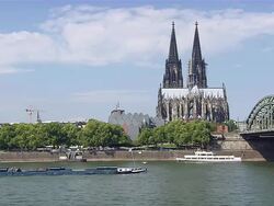 MS Shot of Cologne Cathedral at Old City and transport boat moving under train bridge with Blue sky / Cologne, North Rhine-Westphalia, Germany Stock Footage