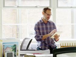 MS smiling mature businessman leaning against table in office workstation working on digital tablet Stock Footage
