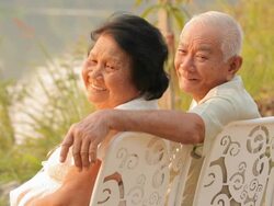 Senior couple sitting near river during sunset Stock Footage