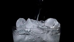 Pouring water into glass of ice with splashes at slow motion on black background Stock Footage