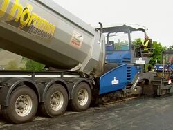MS Shot of dumper unloading material to another machine for road resurfacing and workers working / Saarburg, Rhineland-Palatinate, Germany Stock Footage