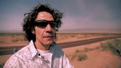 A passenger of a red convertible stands away from the highway and surveys the Nevada desert. Stock Footage