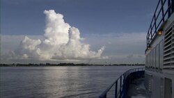 A cloud formation floats above the shoreline as a commercial boat sails on the Mississippi River. Stock Footage