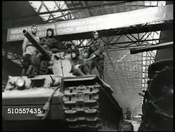 1950: RUSSIAN WEAPONS: INT Warehouse w/ rows of parked tanks w/ two tanks moving forward. LA Tanks moving forward. WS INT Munitions factory. Russian female factory worker checking rifle barrels. Artillery shells moving on hanging warehouse transport. Instructional Video