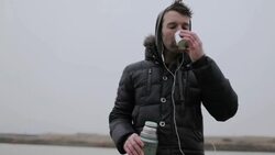 Young man pouring, drinking hot tea on frozen pond in winter in rural Montana, USA. Stock Footage