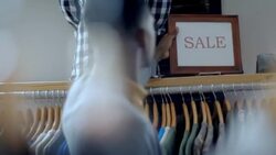 Small business employee places SALE sign on shelf above clothing rack Stock Footage