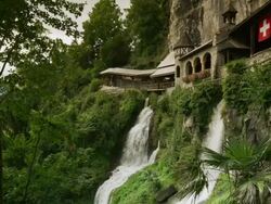 Slow motion/medium shot of waterfall and buildings on cliffs / St. Beatus Caves, Switzerland Stock Footage