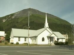 "Seward Memorial United Methodist Church with forested mountain behind, pick-up drives past right to left, 4th Avenue, Seward, Kenai Peninsula, Alaska." Stock Footage