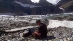 A geologist sits at the base of glaciers and enters data on his laptop in Glacier National Park, Montana. Stock Footage