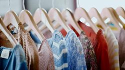 Women's shirts with various patterns and designs hang from rack in modern clothing store Stock Footage