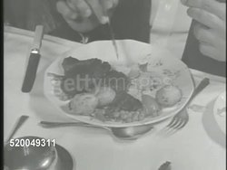 1949: INDIA CLASSES: VS Various upper class people dining at long table, cutting potatoes on dish, FADE TO VS Indian family sitting on floor in home eating rice w/ hands. Rich, poor, social class Instructional Video