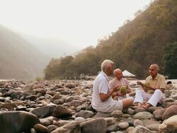 Three senior men drinking coconut water at riverbank, Ganges River, Rishikesh, Uttarakhand, India Stock Footage