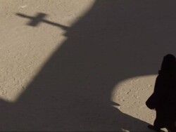 High Angle, static - An Egyptian wears dark robes and walks across the shadow of an archway bearing a cross / Egypt Stock Footage