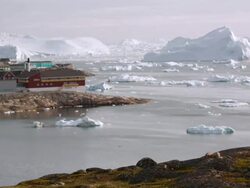 WS T/L View of boats moving in ocean passing icebergs next to coastal town / Ilulissat, Greenland Stock Footage